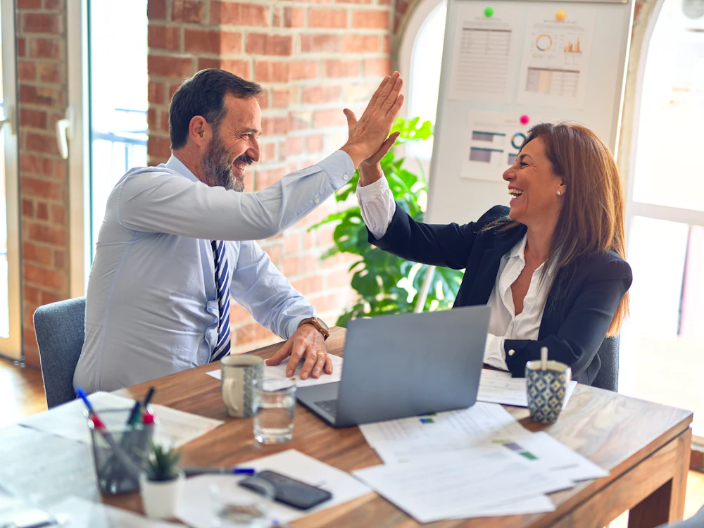 A hiring manager and a new team member celebrating a successful hire in a bright office